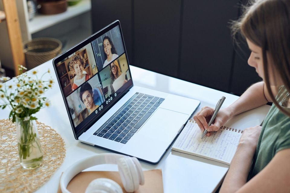 Student taking notes during a video call on a laptop.